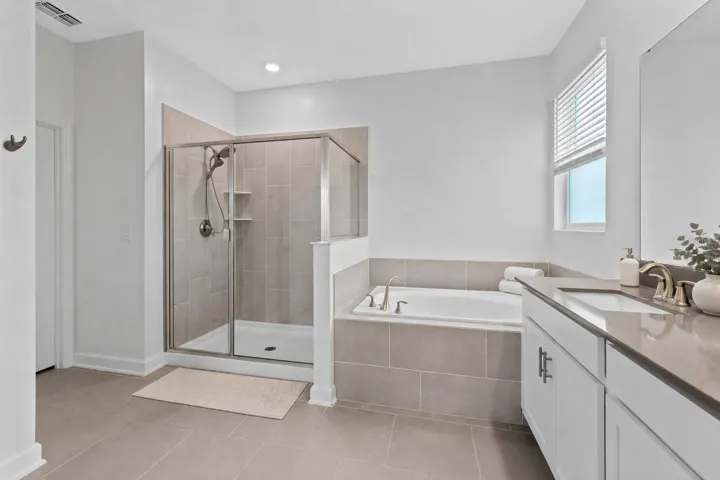 Tucked away at the rear of the home, the primary suite offers a generous walk in closet and a spacious private bathroom complete with quartz countertops, dual sinks, a soaking tub and separate shower. Direct access from the primary suite into the laundry room adds another layer of everyday convenience.