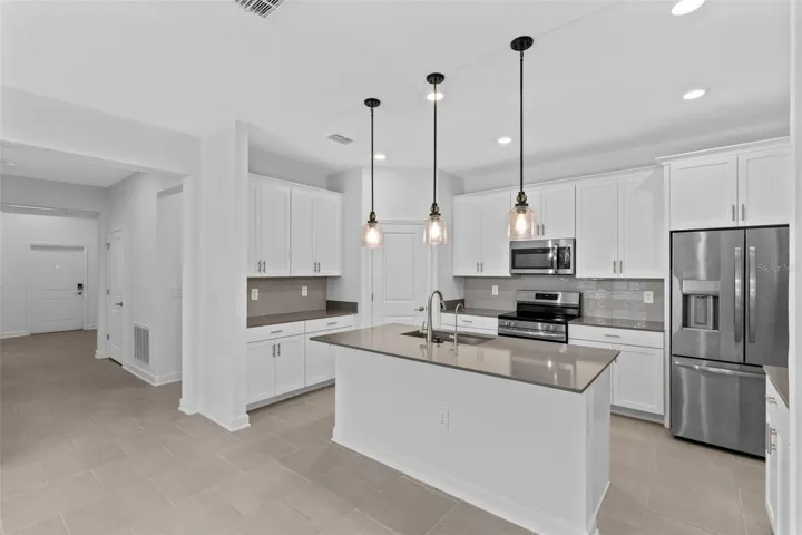 At the heart of the home, the kitchen features shaker style cabinetry, quartz countertops, stainless steel appliances, a tiled backsplash, pantry storage and a large island with breakfast bar seating beneath pendant lighting.