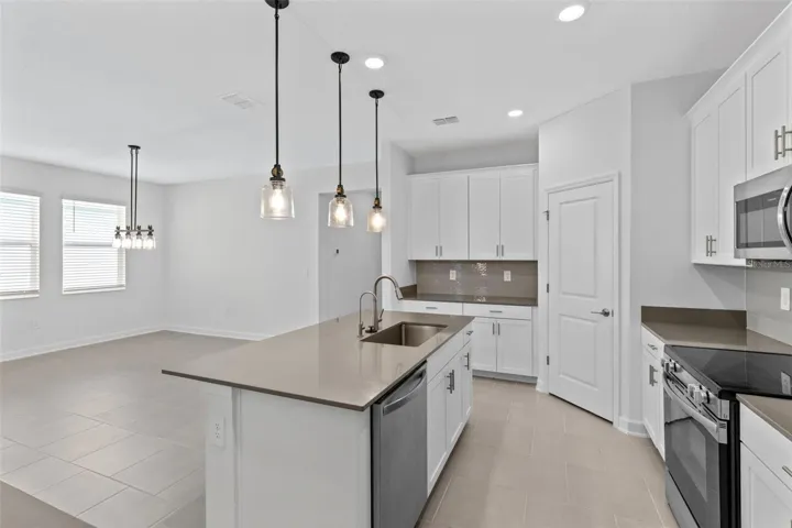 At the heart of the home, the kitchen features shaker style cabinetry, quartz countertops, stainless steel appliances, a tiled backsplash, pantry storage and a large island with breakfast bar seating beneath pendant lighting.