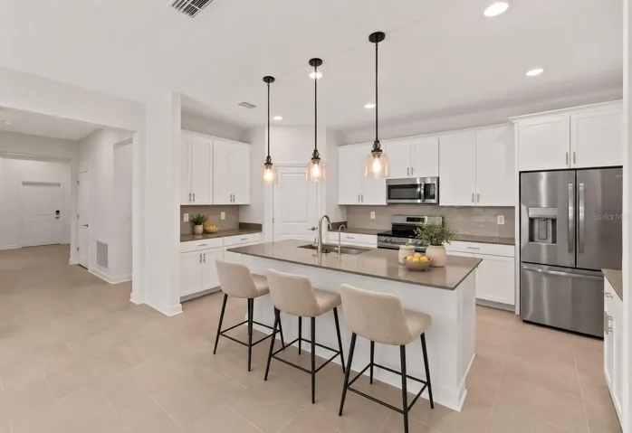 At the heart of the home, the kitchen features shaker style cabinetry, quartz countertops, stainless steel appliances, a tiled backsplash, pantry storage and a large island with breakfast bar seating beneath pendant lighting.
