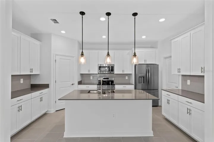 At the heart of the home, the kitchen features shaker style cabinetry, quartz countertops, stainless steel appliances, a tiled backsplash, pantry storage and a large island with breakfast bar seating beneath pendant lighting.
