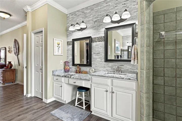 The east vanity has stone countertops, a makeup area, elevated sink, stone wall with accents, upgrades lighting and plumbing fixtures.