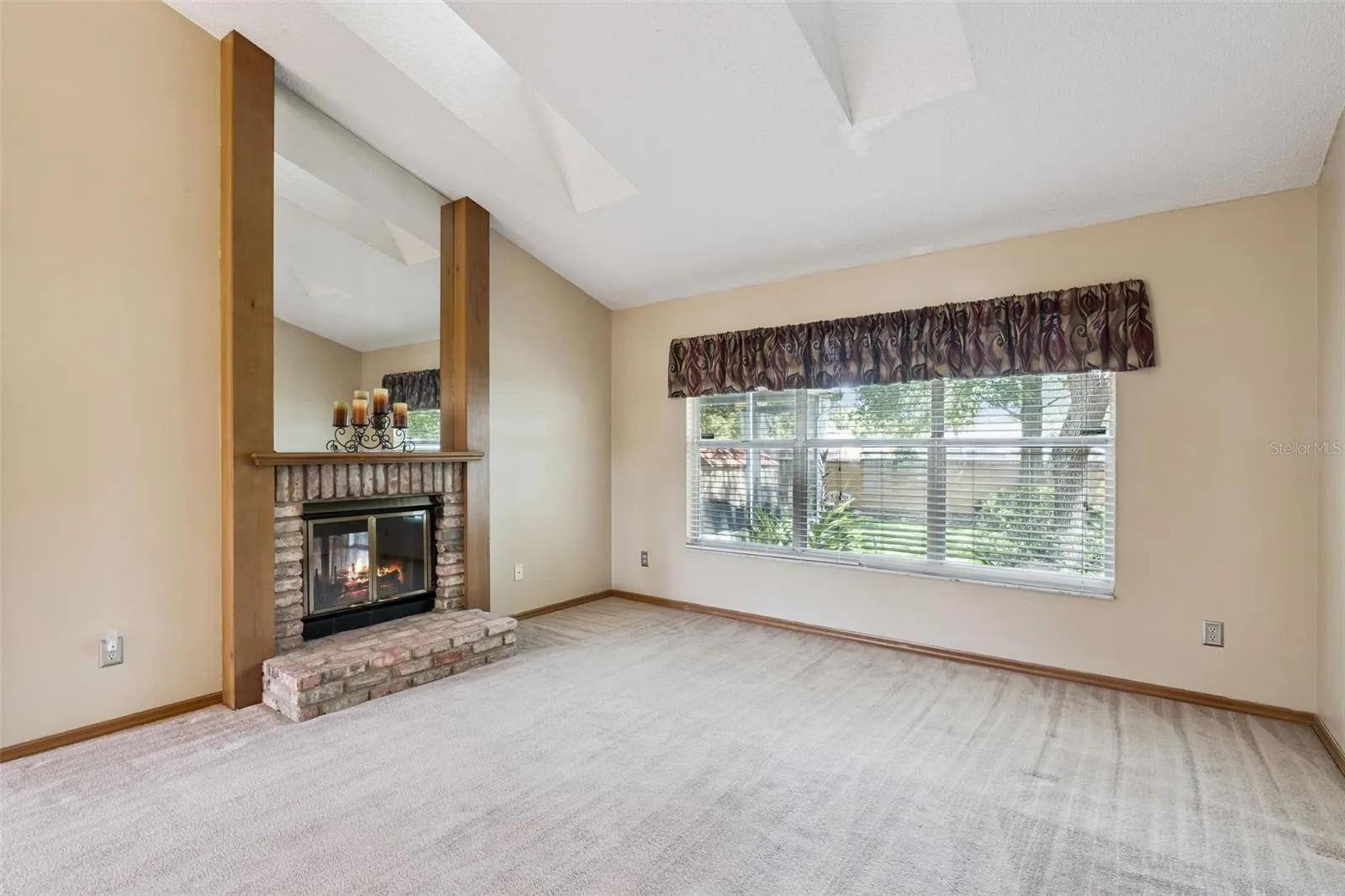 Inviting living room with double-sided brick fireplace, skylights and a peaceful backyard view