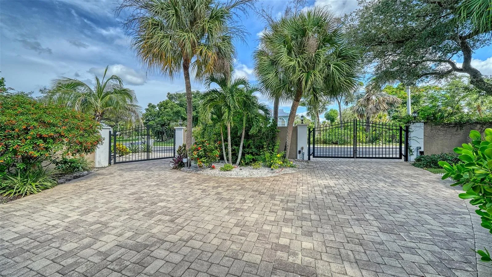 Circular paver driveway and gated entrance framed by mature palms and tropical landscaping.