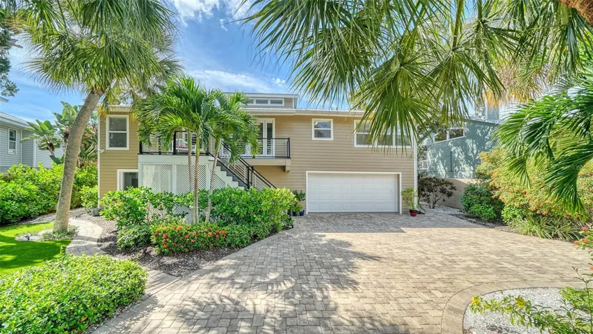 Elevated Key West style home with mature tropical landscaping and an oversized two-car garage.