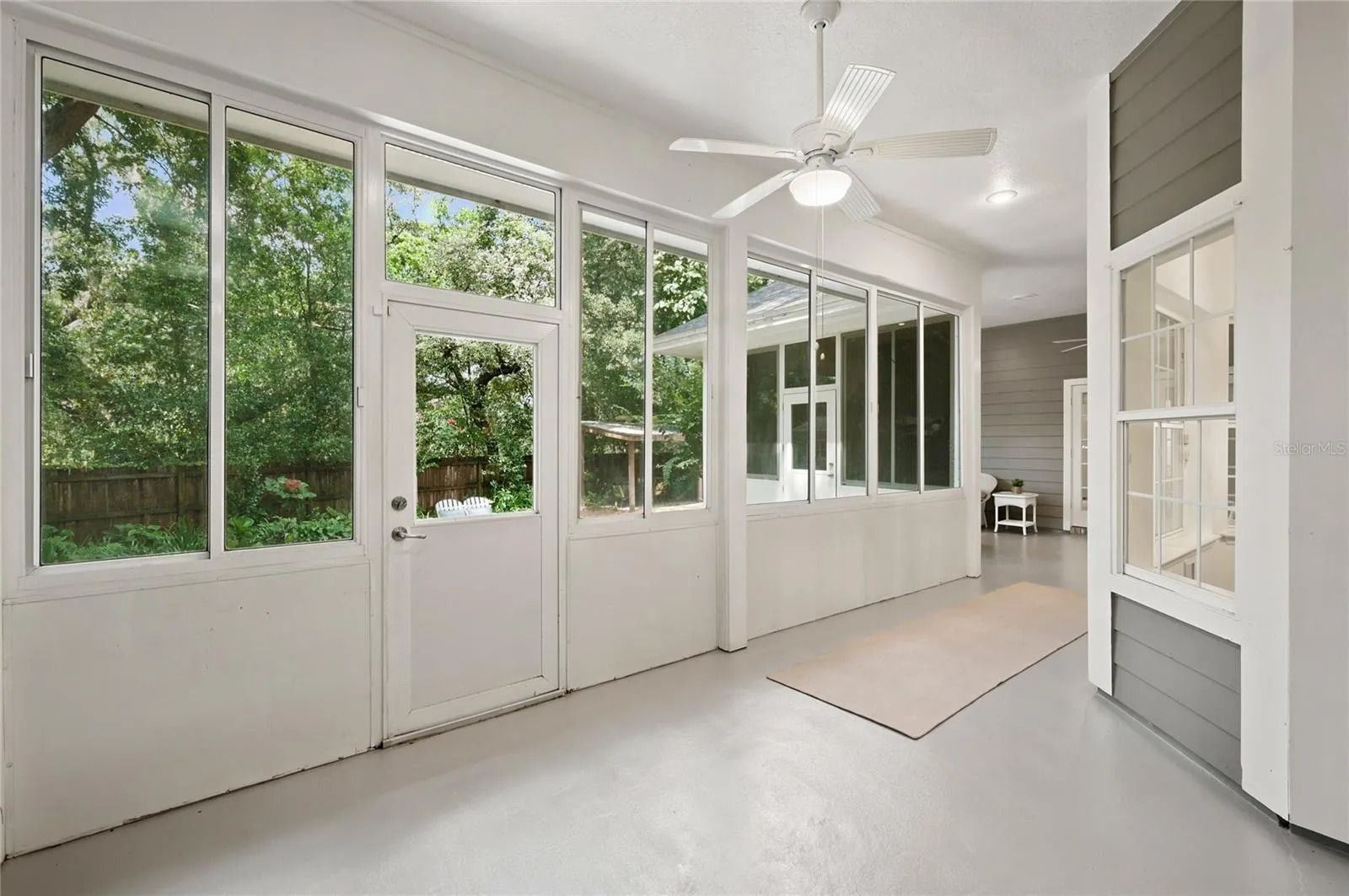 An impressive porch extends the home’s living space, offering a light-filled, breezy retreat with walls of windows, ceiling fans, and peaceful views of the lush backyard.