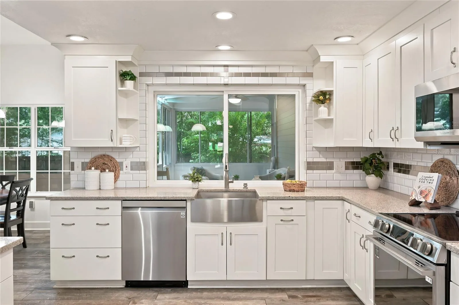 Kitchen showcases subway tile backsplash design, stainless steel appliances, a stainless farmhouse sink beneath pass through window for serving in the enclosed porch.