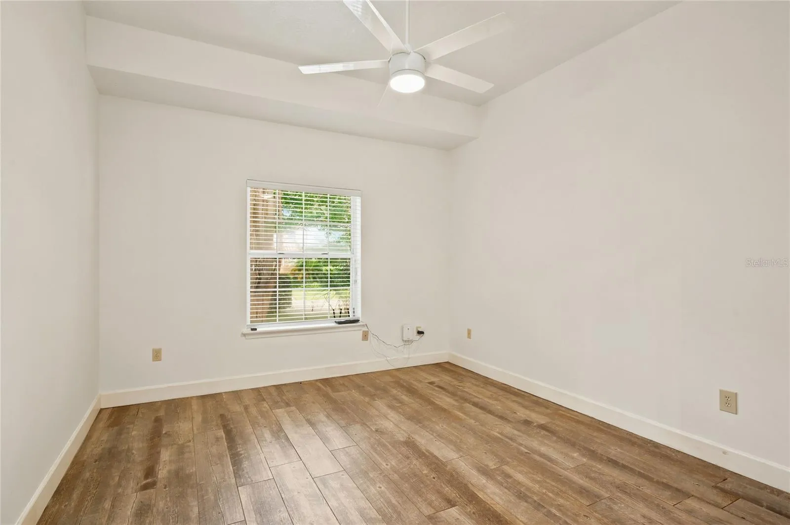Bedroom 2 is generously sized, featuring high ceilings, ceiling fan, wood-look flooring, and a large window that fills the room with natural light.