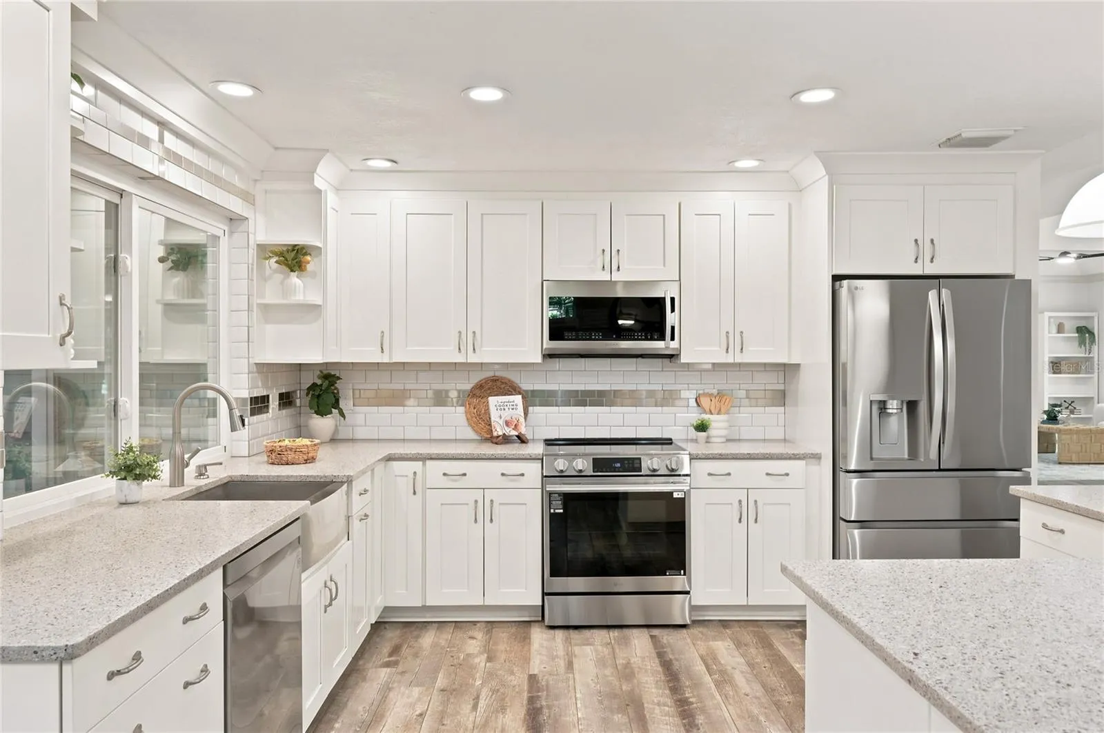 A bright, beautifully updated kitchen features crisp white cabinetry, stone countertops, &amp; stainless steel appliances