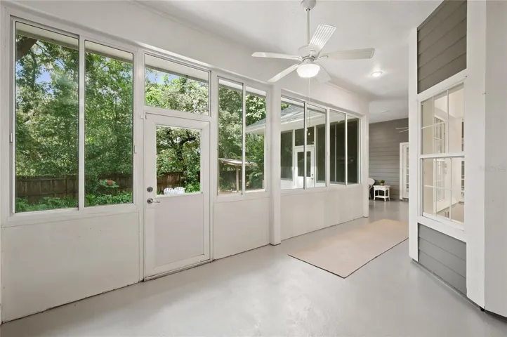An impressive porch extends the home’s living space, offering a light-filled, breezy retreat with walls of windows, ceiling fans, and peaceful views of the lush backyard.