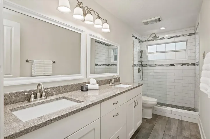 Updated guest bath features a spacious dual-sink vanity, granite countertops, and a glass-enclosed walk-in shower with stylish tile accents.