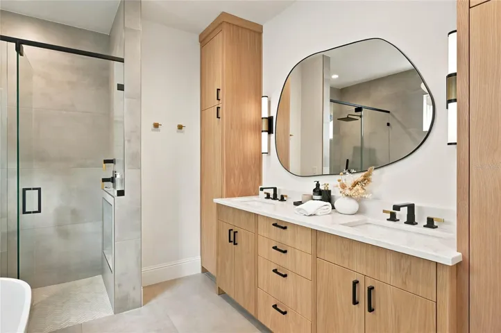 pairs warm wood cabinetry with clean contemporary finishes featuring a double vanity accented by mixed black and brass fixtures. A statement mirror &amp; lighting add an artful touch to the serene, sophisticated space.