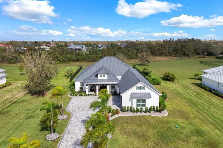 Aerial view of the property with long paver driveway, metal roof, custom landscaping and nature preserve behind the home adding additional privacy.