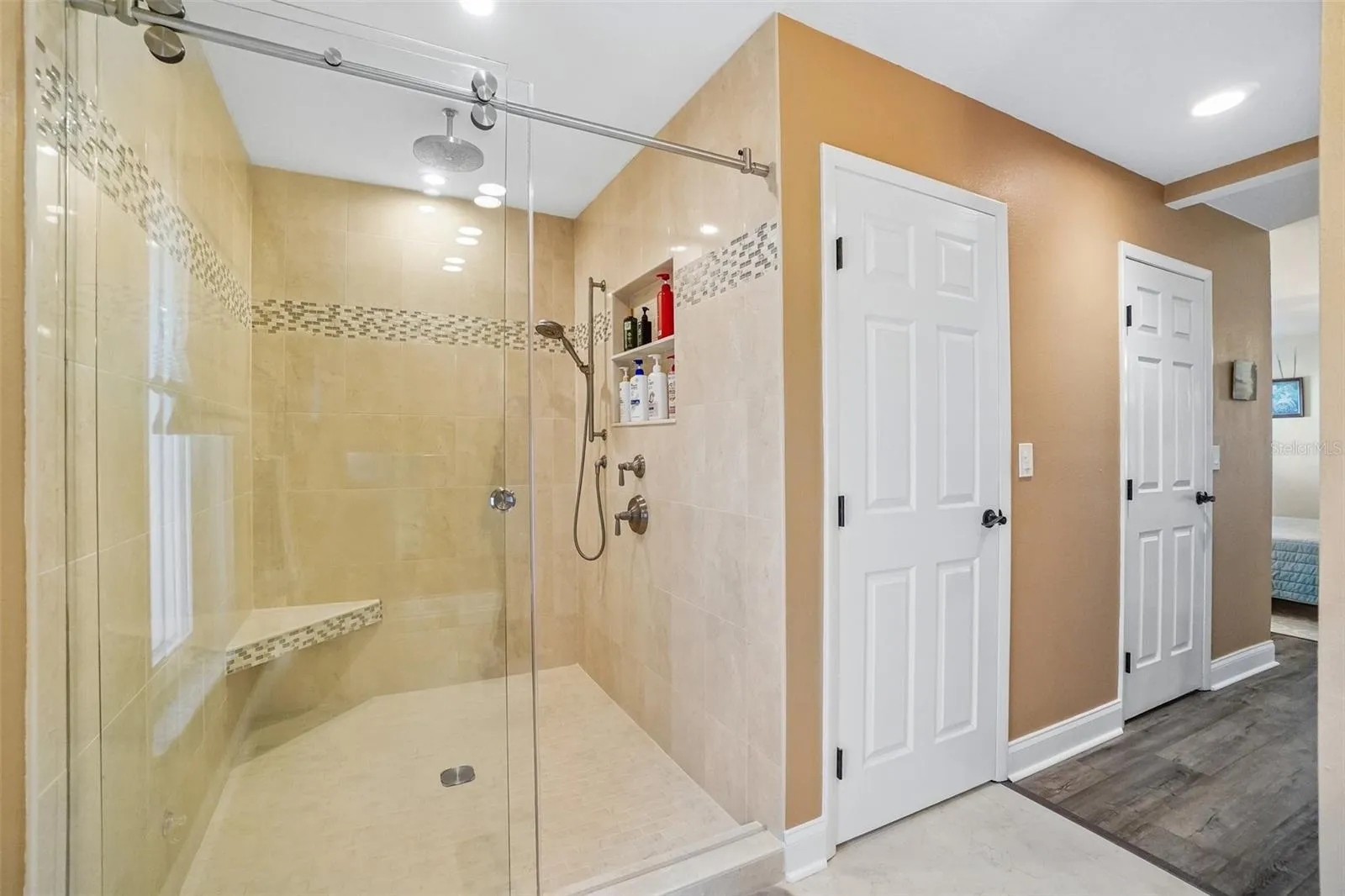 Primary Ensuite Bathroom – The primary bath features a large walk-in shower with frameless glass, full-height tile, a decorative mosaic accent band, built-in bench, rainfall showerhead, and handheld shower fixture.