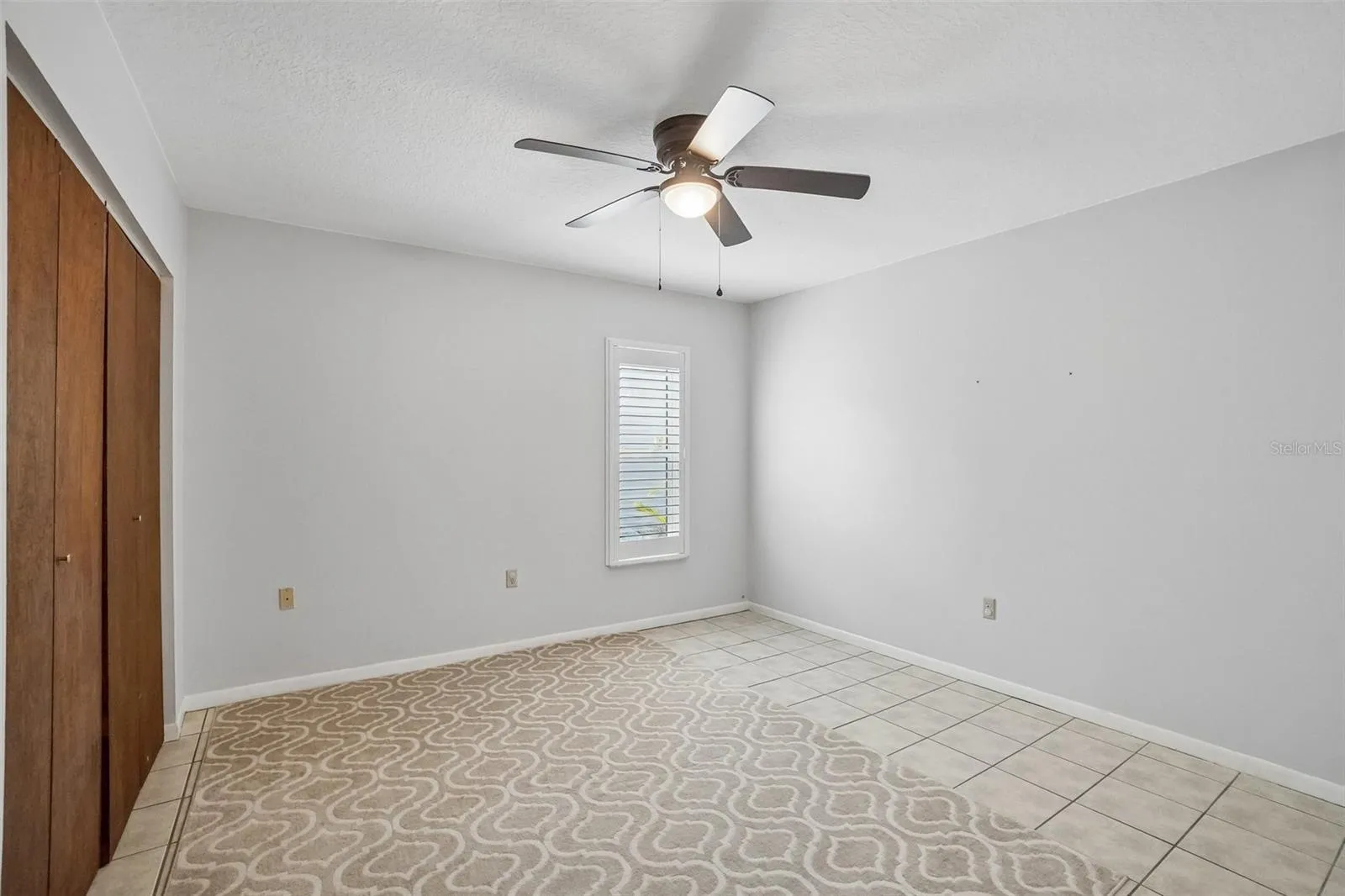Third Bedroom – The third bedroom offers neutral finishes, tile flooring, a ceiling fan, a plantation-shuttered window, and a wide sliding-door closet for generous storage.