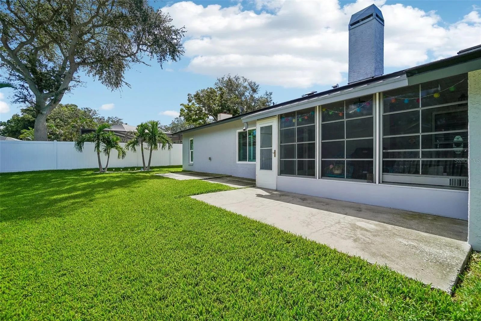 Rear Patio & Backyard – Showcasing the enclosed patio and adjoining concrete patio area, with the manicured lawn and privacy fencing extending beyond.