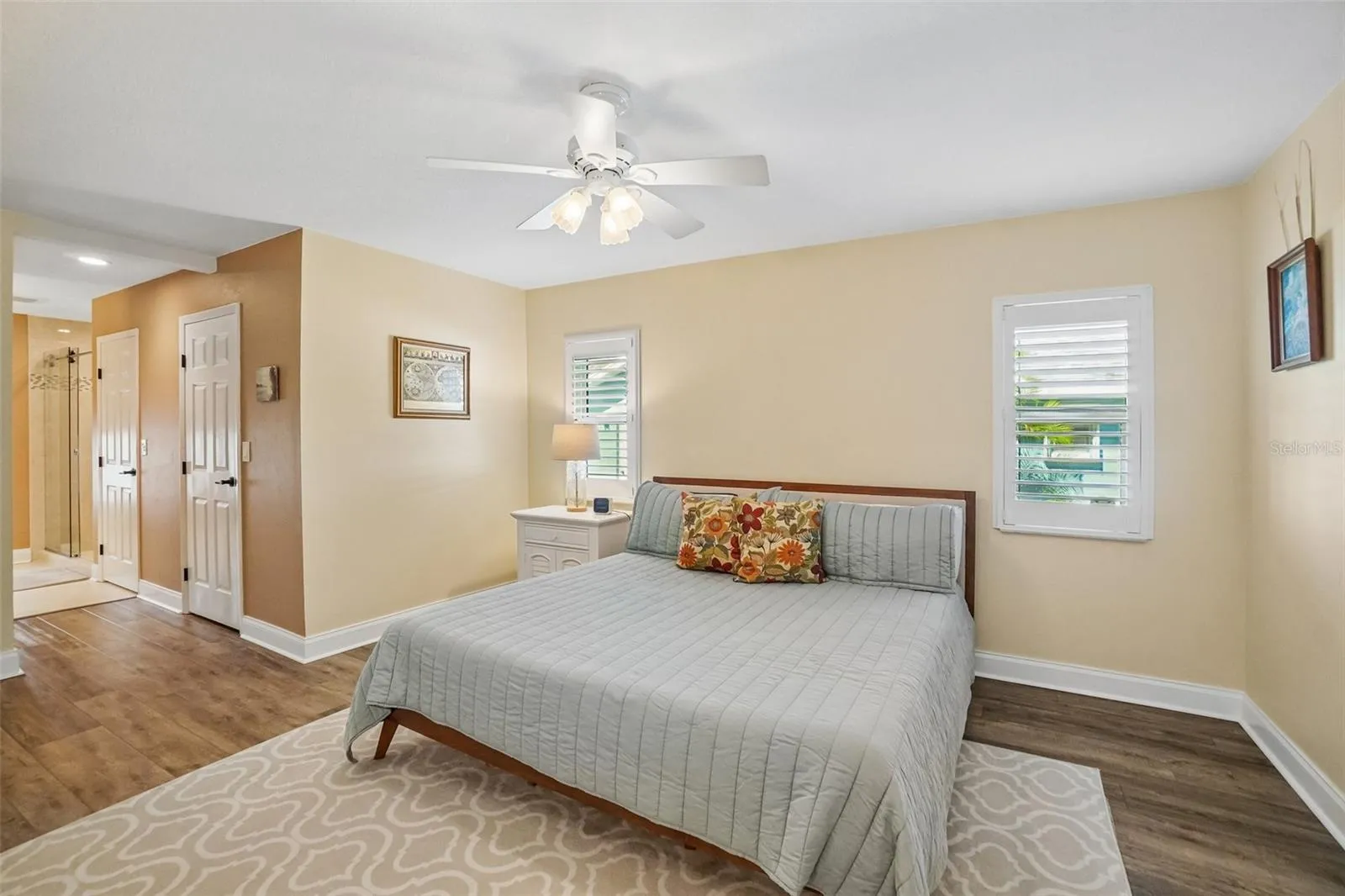 Primary Bedroom – Another view highlights the room’s generous proportions, dual shuttered windows, ceiling fan, and convenient access toward the adjoining bath and closet areas.