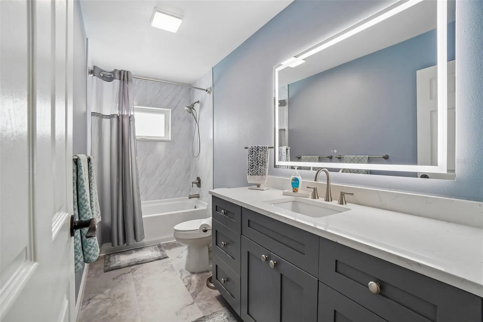 Second Bathroom – The second full bath features a dark shaker-style vanity with a light countertop, an illuminated mirror, and a tub/shower combination with a clean, contemporary surround.