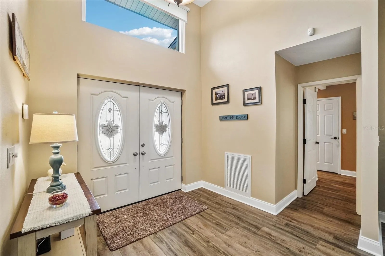 Foyer – Decorative double entry doors and a high transom window create a bright, welcoming arrival, complemented by wood-look flooring and easy access to the adjoining living spaces.