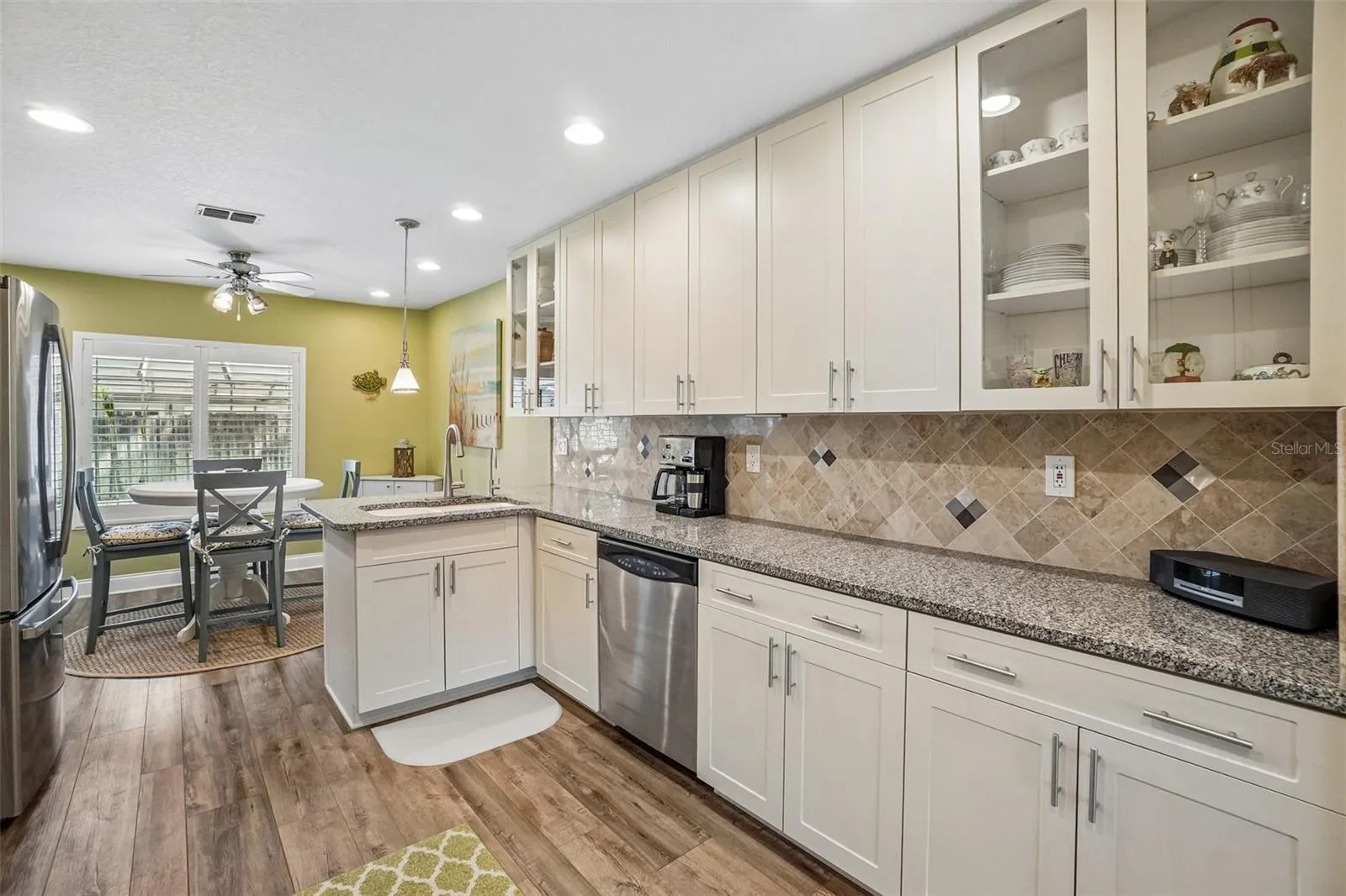 Kitchen – Another kitchen view highlights generous counter space, plentiful cabinetry including glass-front display cabinets, stainless steel appliances, and an open connection to the breakfast nook.