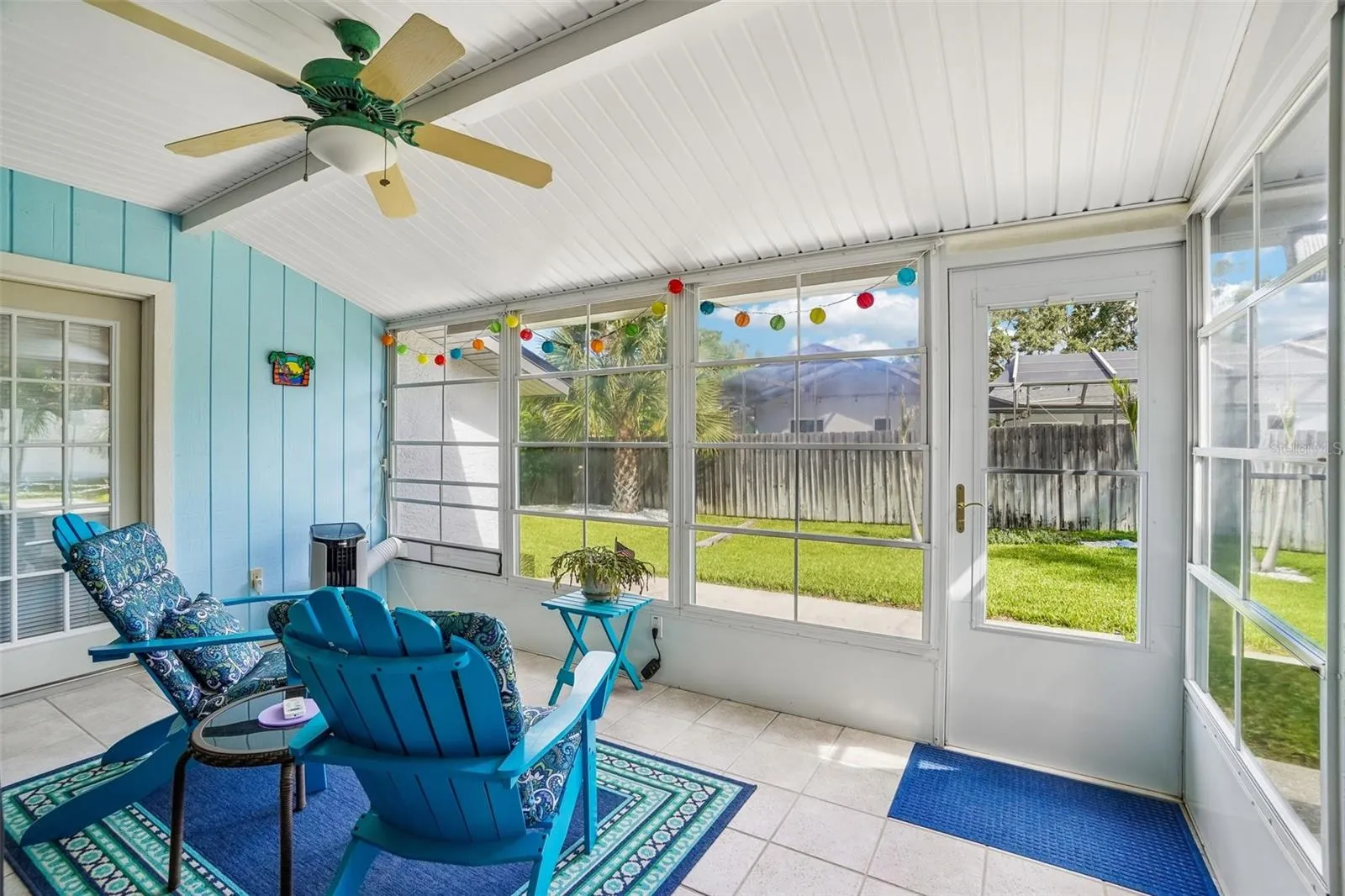 Enclosed Rear Patio – The bright enclosed rear patio offers tiled flooring, a ceiling fan, expansive screened/windowed walls, and direct access to the backyard for relaxed indoor-outdoor living.