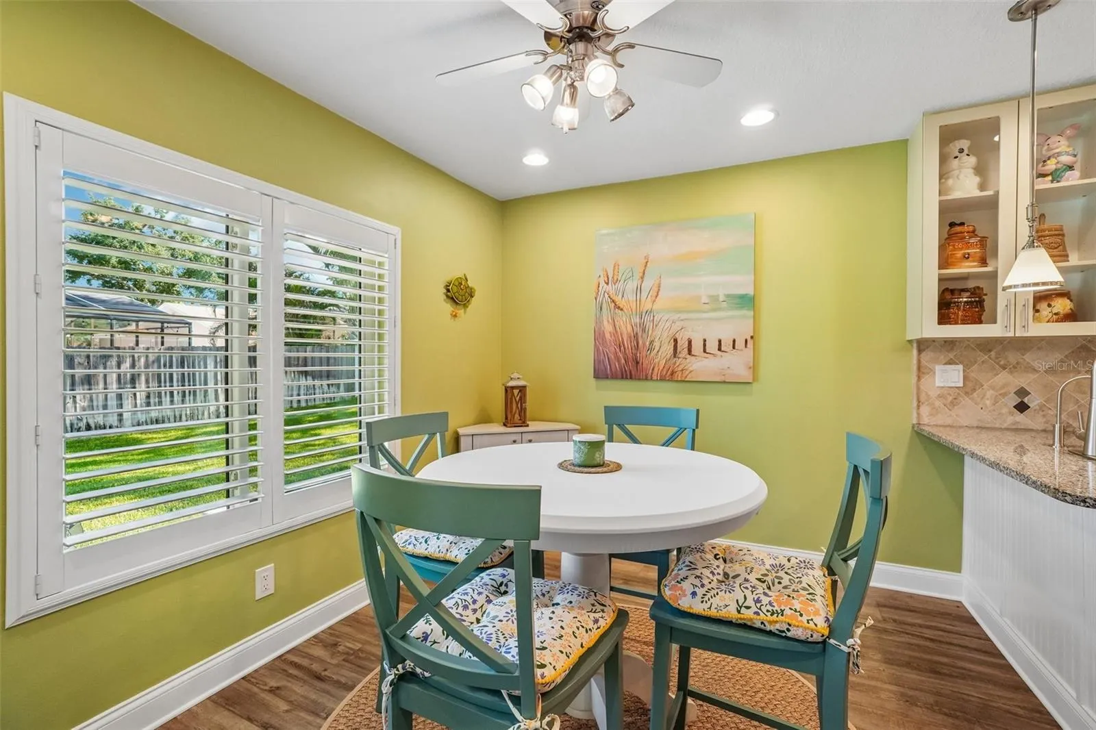 Breakfast Nook – The bright breakfast nook features a large shuttered window overlooking the yard, wood-look flooring, and a ceiling fan, with convenient access to the adjoining kitchen.