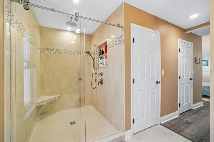 Primary Ensuite Bathroom – The primary bath features a large walk-in shower with frameless glass, full-height tile, a decorative mosaic accent band, built-in bench, rainfall showerhead, and handheld shower fixture.