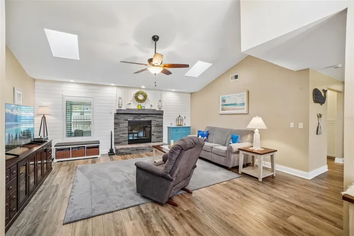 Living Room – The spacious living room features a vaulted ceiling with skylights, wood-look flooring, and a striking stacked-stone fireplace set against a white shiplap accent wall.