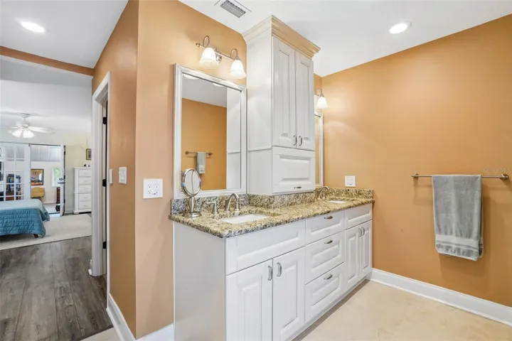 Primary Ensuite Bathroom – The primary ensuite features a spacious dual-sink vanity with granite countertops, abundant white cabinetry, a tall center storage cabinet, and bright vanity lighting.