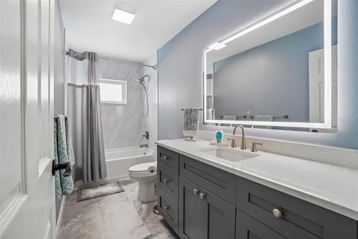 Second Bathroom – The second full bath features a dark shaker-style vanity with a light countertop, an illuminated mirror, and a tub/shower combination with a clean, contemporary surround.