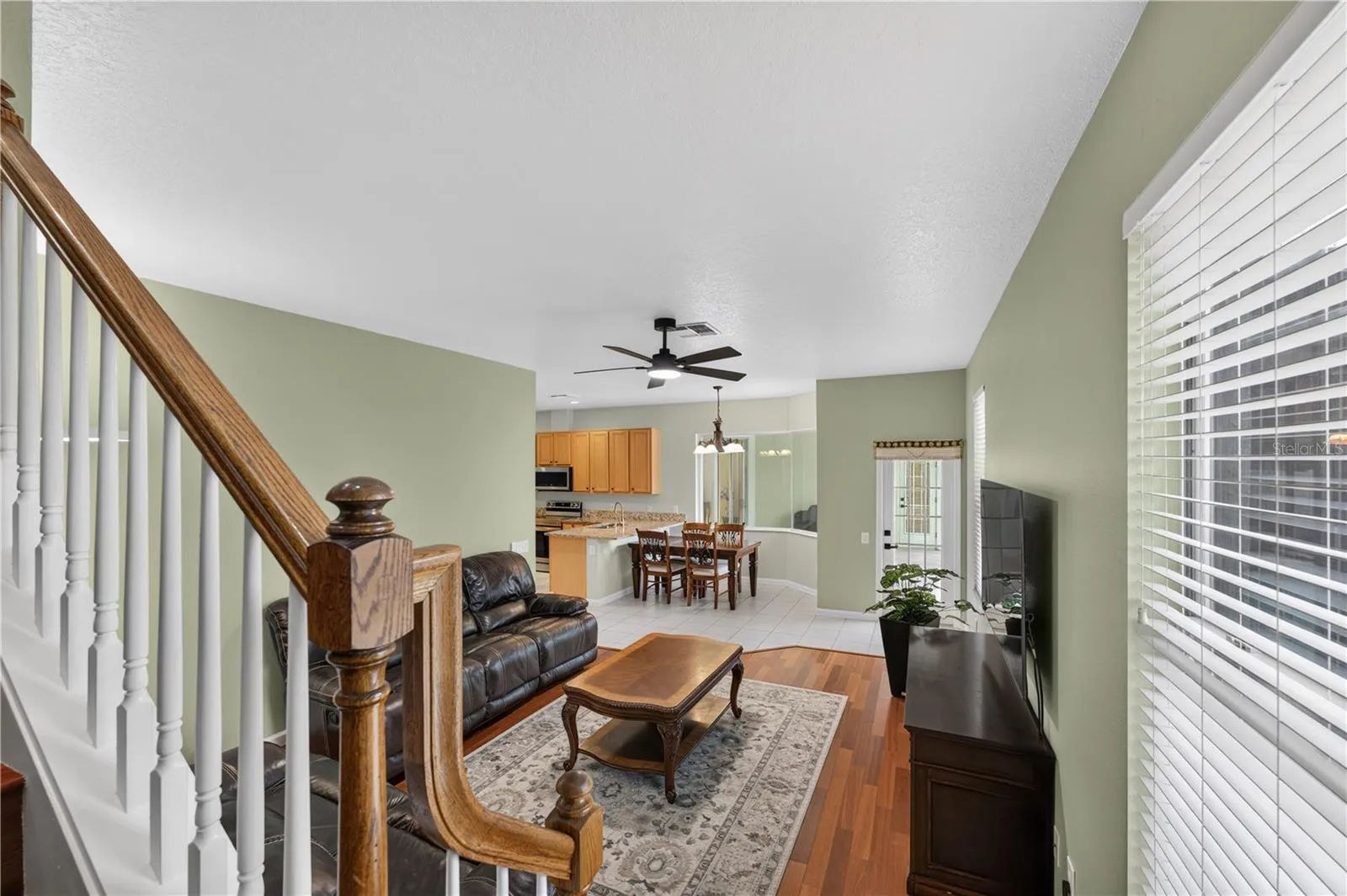 Spacious family room featuring high ceilings, a ceiling fan, wood flooring, and an open layout that flows into the dinette and kitchen.
