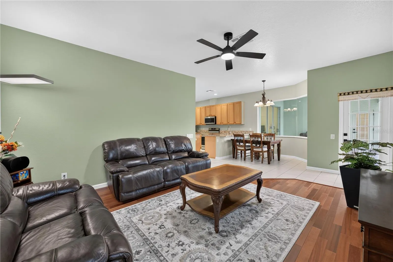 Spacious family room featuring high ceilings, a ceiling fan, wood flooring, and an open layout that flows into the dinette and kitchen.
