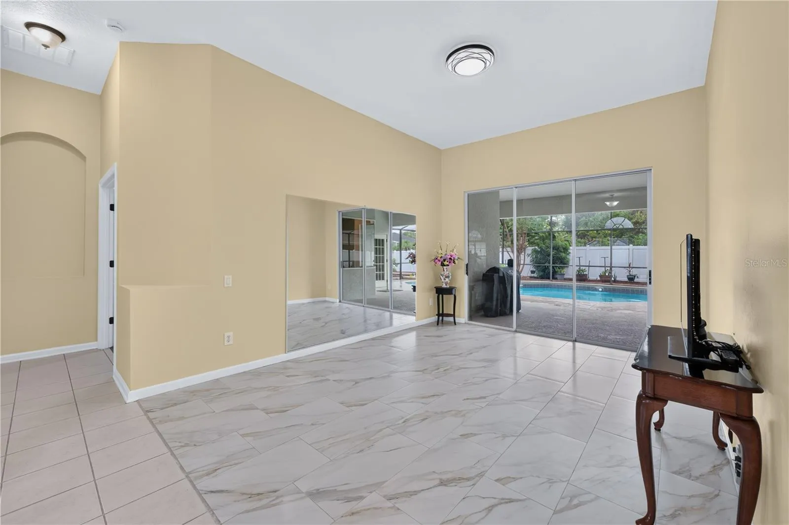 Spacious living room with high ceilings, tile flooring, and sliding glass doors providing direct access to the pool.