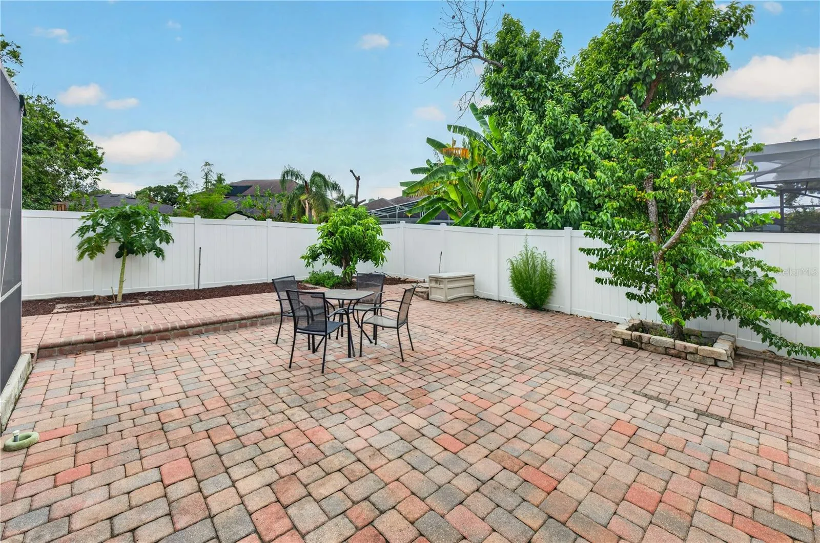 Fenced backyard with an expansive paver patio, mature landscaping, and plenty of room for outdoor entertainment.