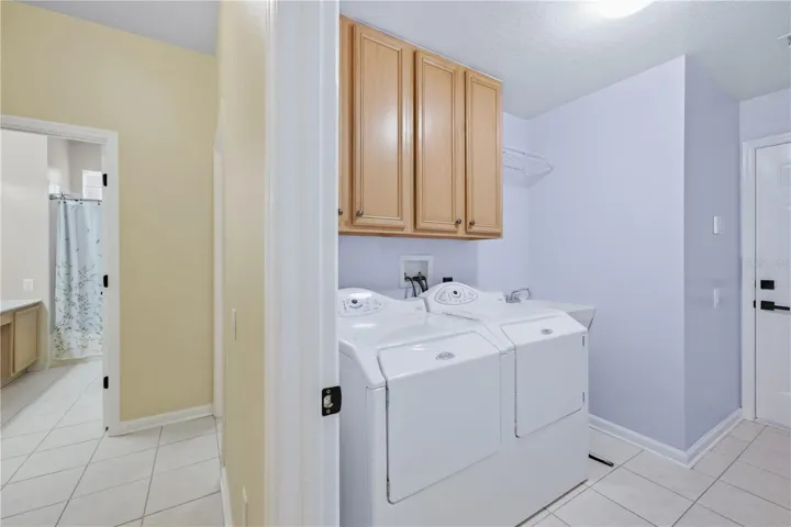 Convenient laundry room with overhead cabinets for additional storage and a utility sink for added functionality.
