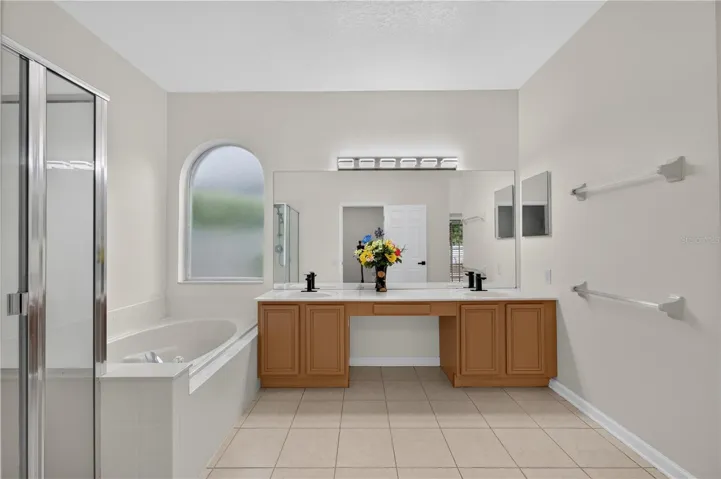 Primary bathroom featuring a garden tub, separate walk in shower, dual sinks, and direct access to the pool area.