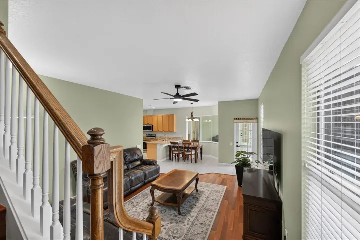 Spacious family room featuring high ceilings, a ceiling fan, wood flooring, and an open layout that flows into the dinette and kitchen.