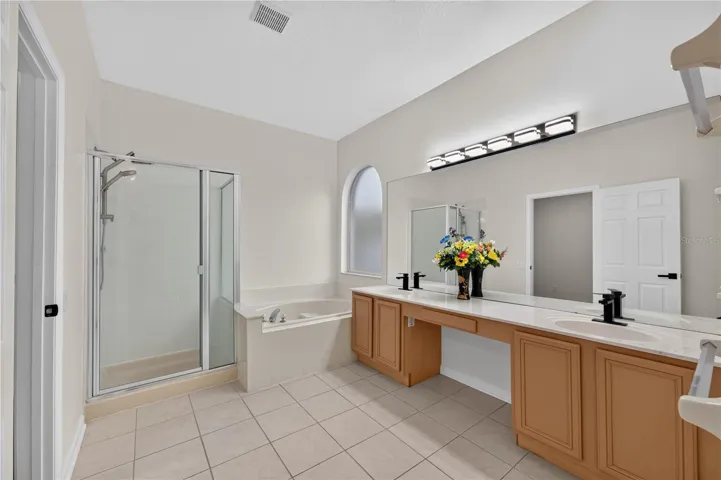 Primary bathroom featuring a garden tub, separate walk in shower, dual sinks, and direct access to the pool area.
