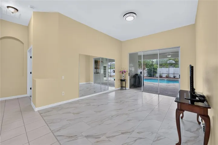 Spacious living room with high ceilings, tile flooring, and sliding glass doors providing direct access to the pool.