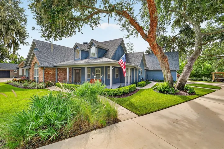 Angled side view of the front of house with covered wraparound front porch under an arching oak tree,