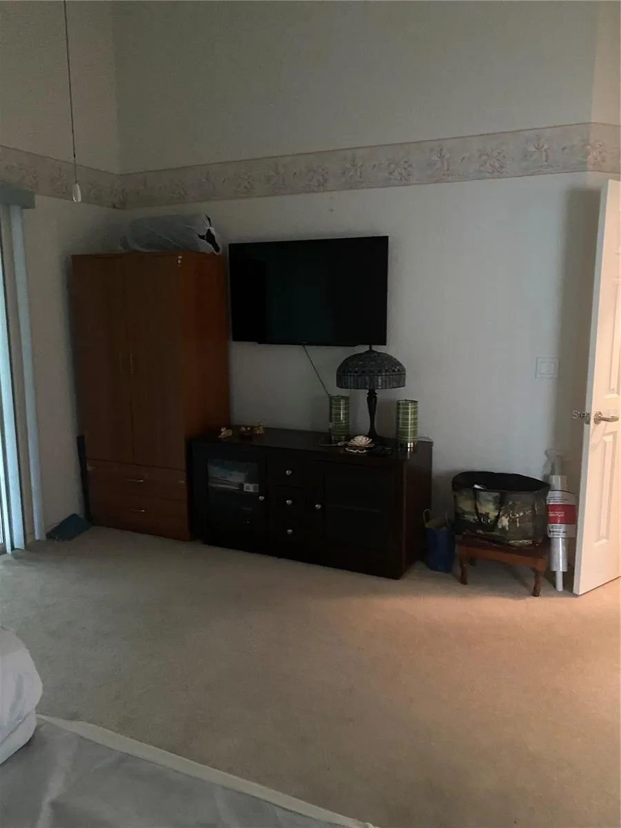 Primary bedroom area, large room, high ceiling, carpeting and sliding glass door.