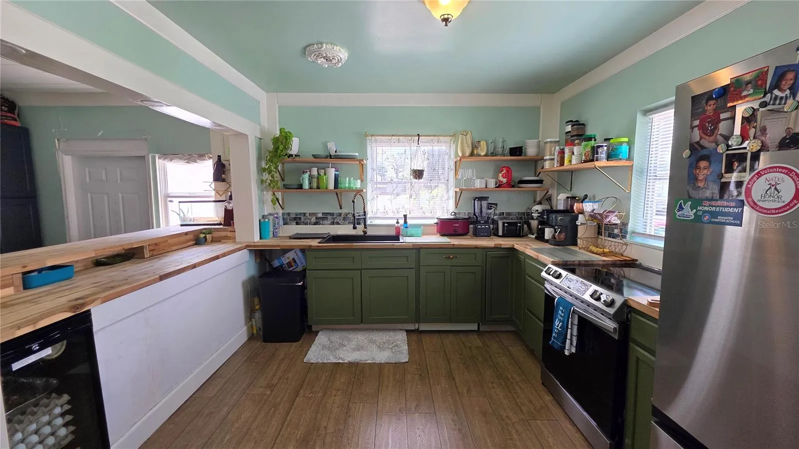 Kitchen with Butcher Block Countertops, Stainless appliances, Decorative Shelving, 2 Windows, and Laminate Flooring