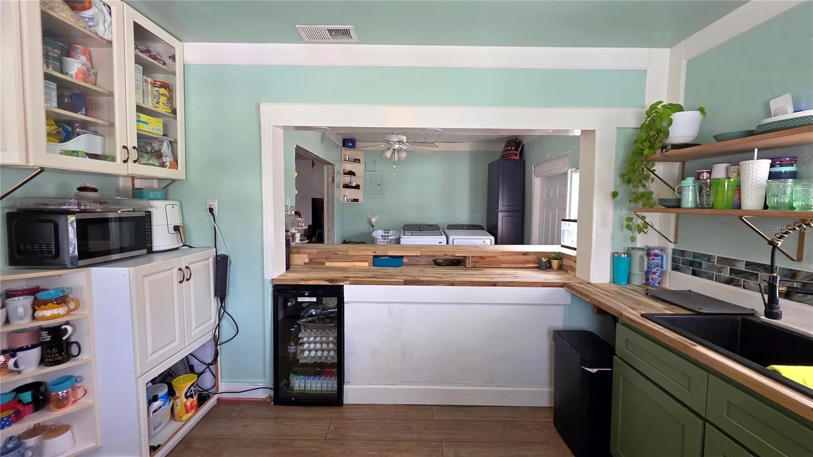 Kitchen Pass Through area to Breakfast Bar Seating, with Butcher Block Countertops, Stainless appliances, Decorative Shelving, 2 Windows, and Laminate Flooring
