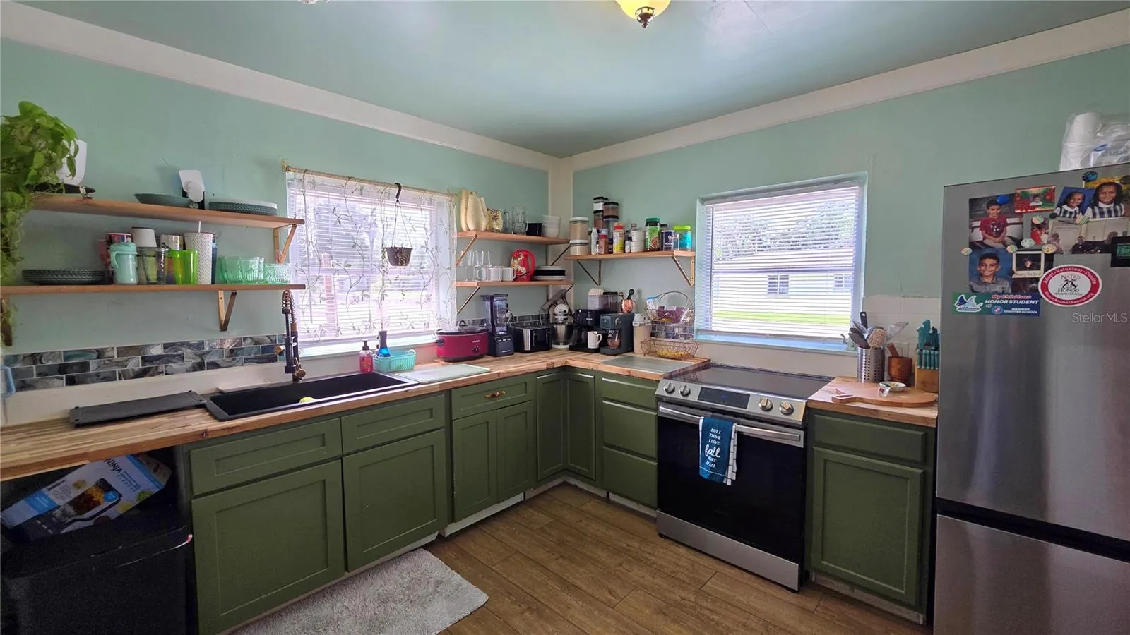Kitchen with Butcher Block Countertops, Stainless appliances, Undermount Sink, Decorative Shelving, 2 Windows, and Laminate Flooring