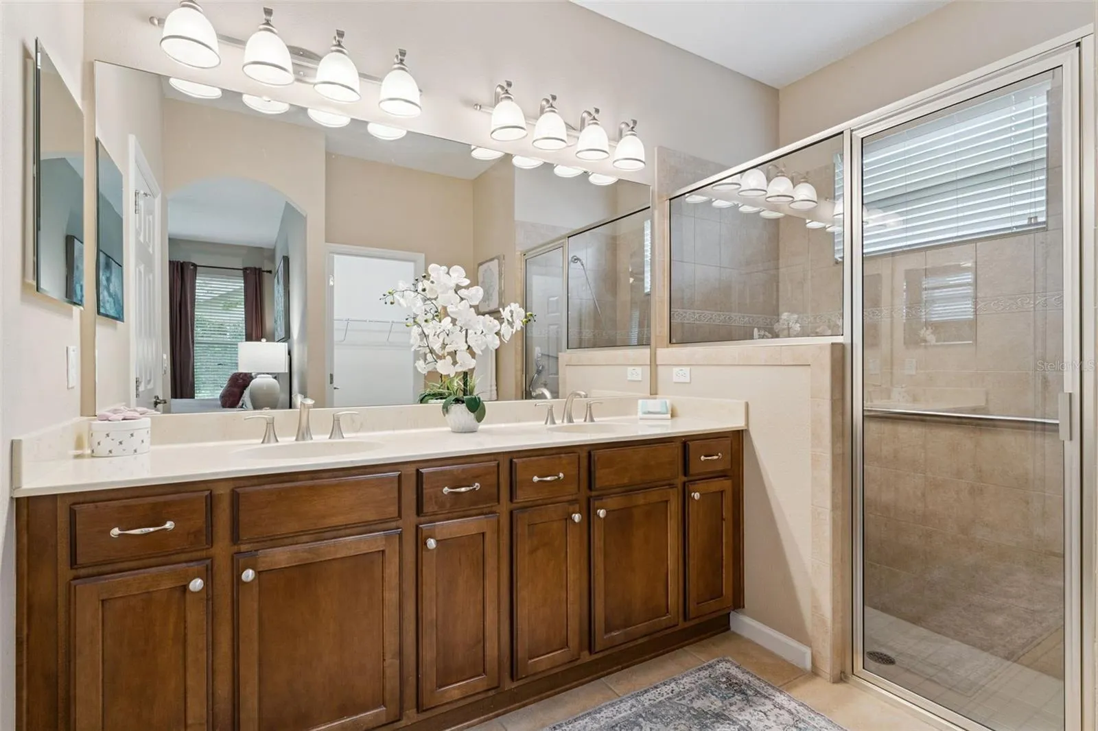 Primary Bathroom w/ dual sinks, glass enclosed walk-in shower, built-in bench seat & a grab bar