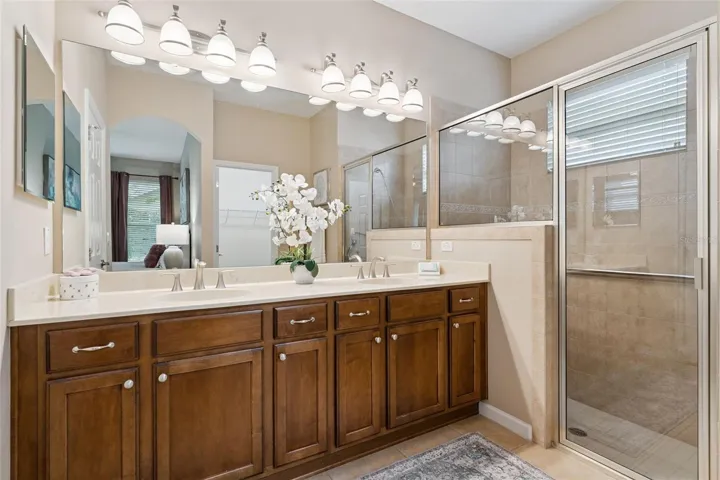 Primary Bathroom w/ dual sinks, glass enclosed walk-in shower, built-in bench seat & a grab bar