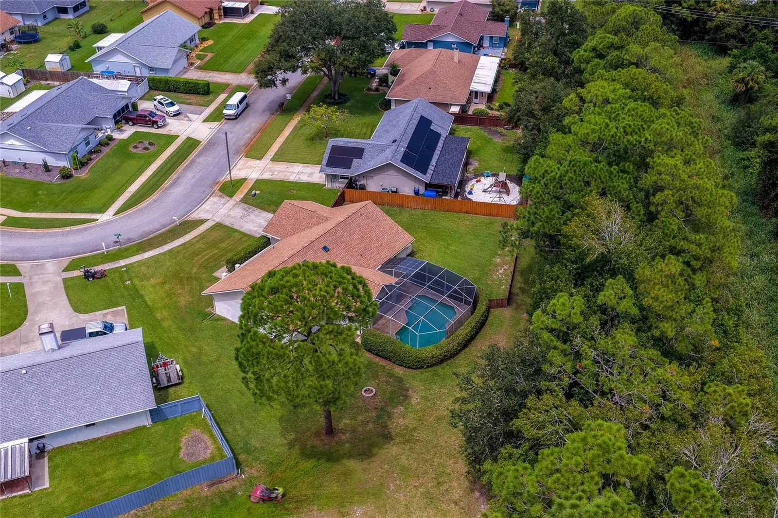 Bird’s-eye view focusing on the backyard pool structure, large lawn, and dense tree-lined privacy buffer.
