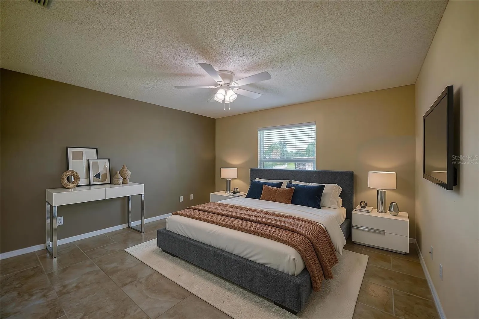 Virtually Staged - Generous bedroom featuring neutral tiled flooring, dual-tone walls, and a central ceiling fan with integrated lighting. Large window with blinds allows for ample natural light.