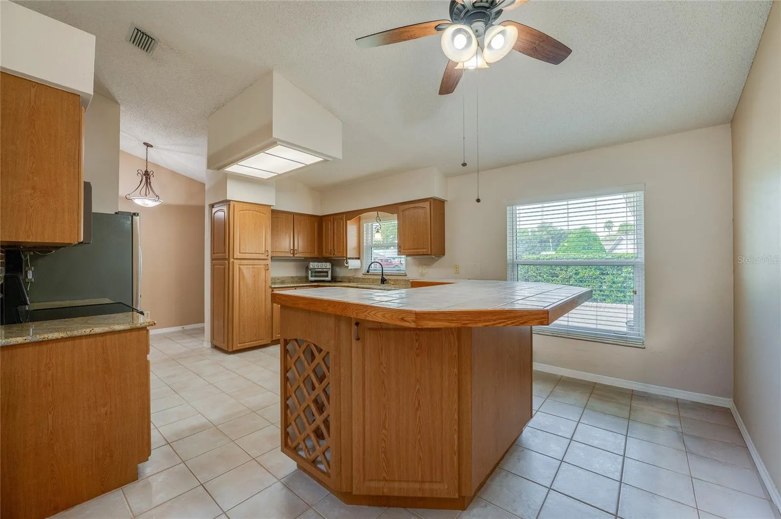 Spacious kitchen displaying warm wooden cabinetry, a tiled center island with built-in wine storage, tile flooring, and a bright window over the sink.