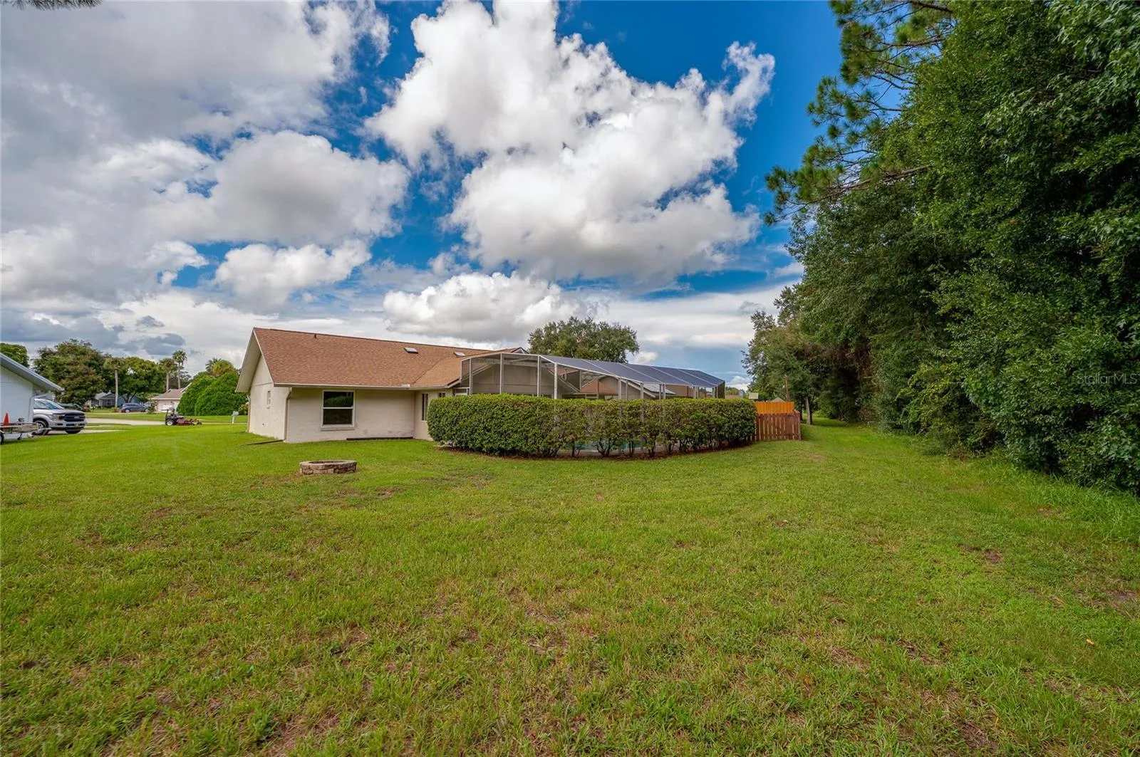 Wide view of the open lawn framing the rear exterior of the home, complete with lush green grass and mature privacy landscaping.